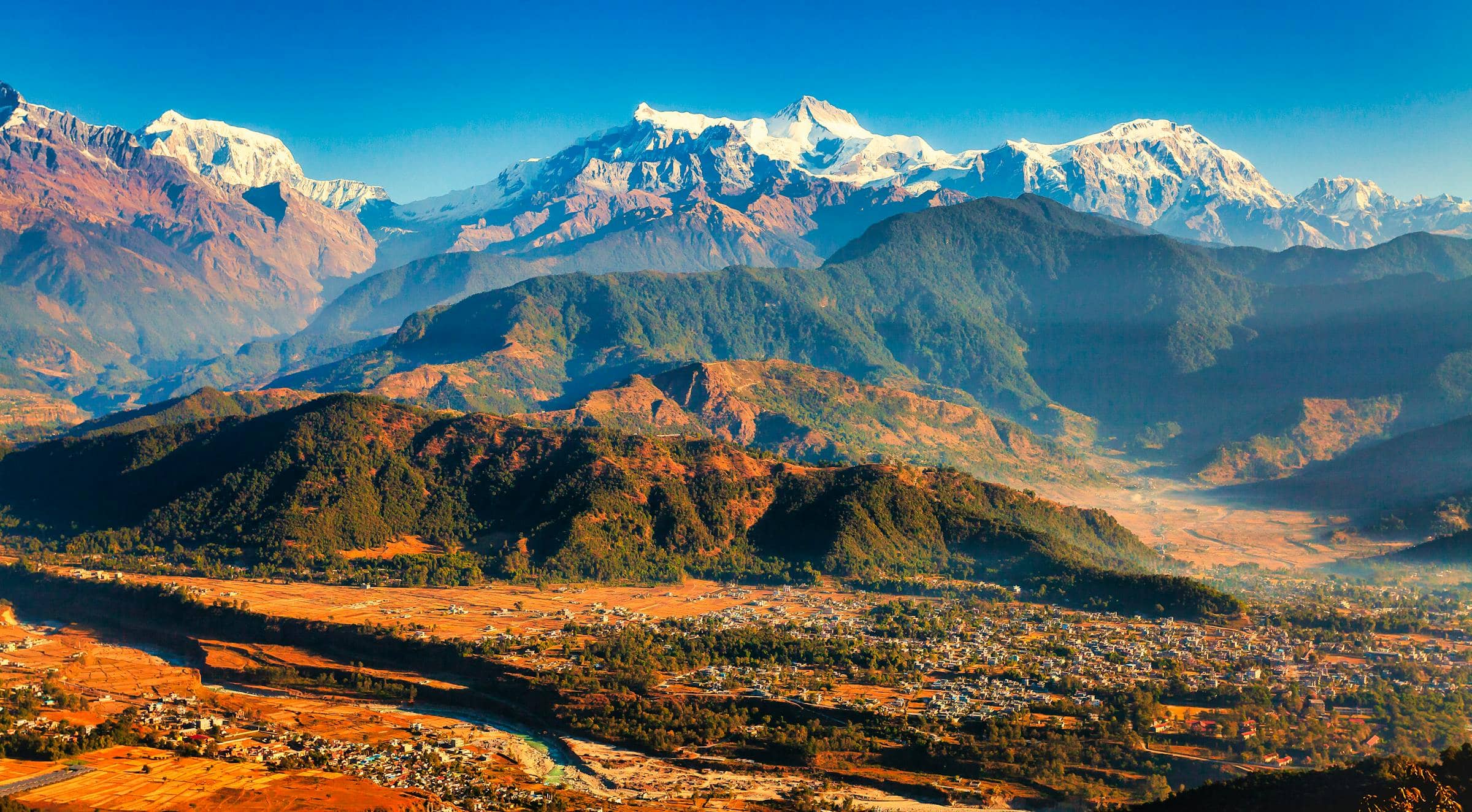 Snow-capped Annapurna peaks rising above terraced green valleys and forested foothills, Pokhara, Nepal.